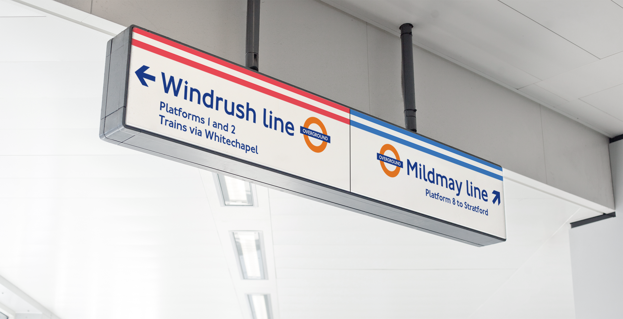A photography of a piece of signage from a London Overground station: a wide horizontal sign held by a metal box hanging from a ceiling. The sign has two sections, showing directions for two different London Overground lines (Windrush and Mildmay). The sign incudes dual lines in the respective service colours and London Overground logos next to the line names.